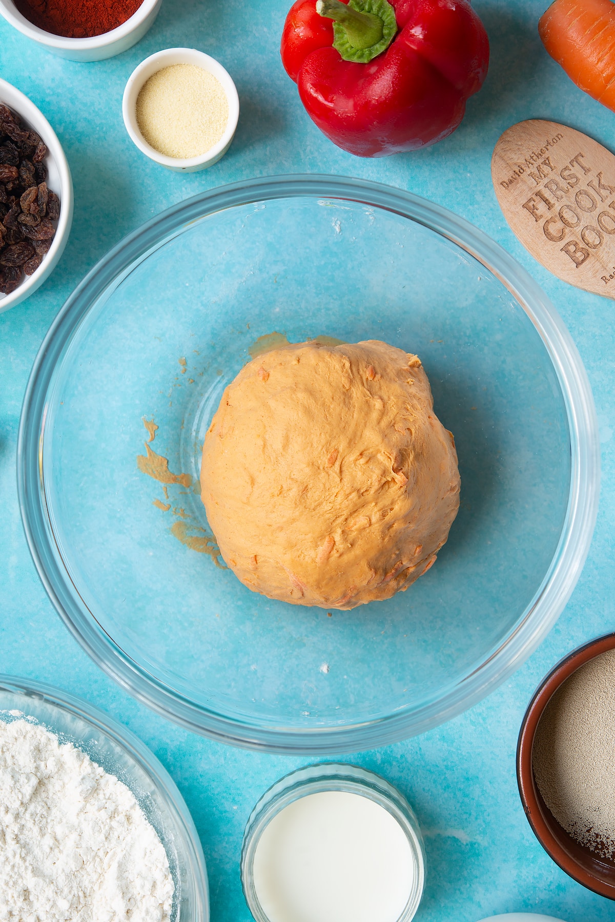 Kneaded paprika and carrot bread dough in a bowl. Ingredients to make bread snakes surround the bowl.