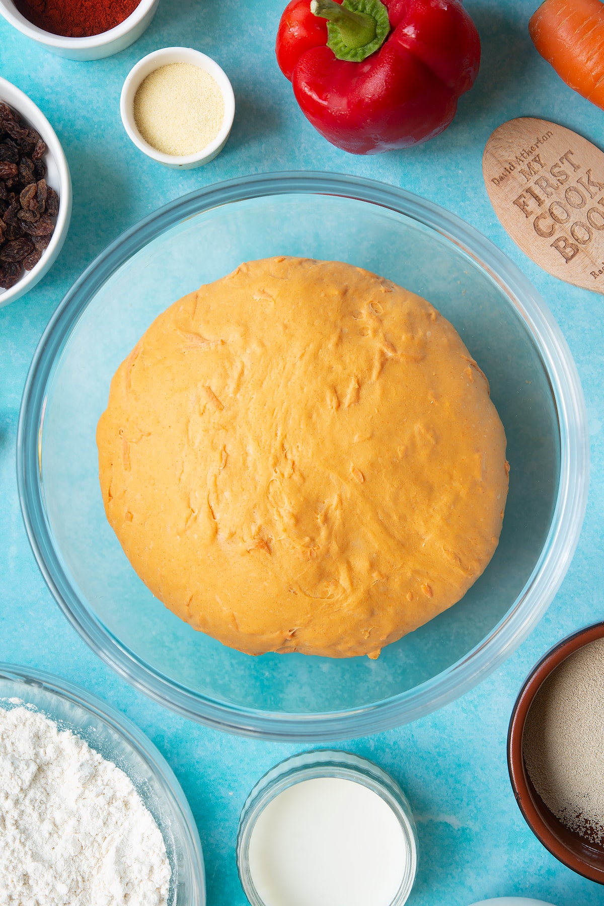 Proved paprika and carrot bread dough in a bowl. Ingredients to make bread snakes surround the bowl.