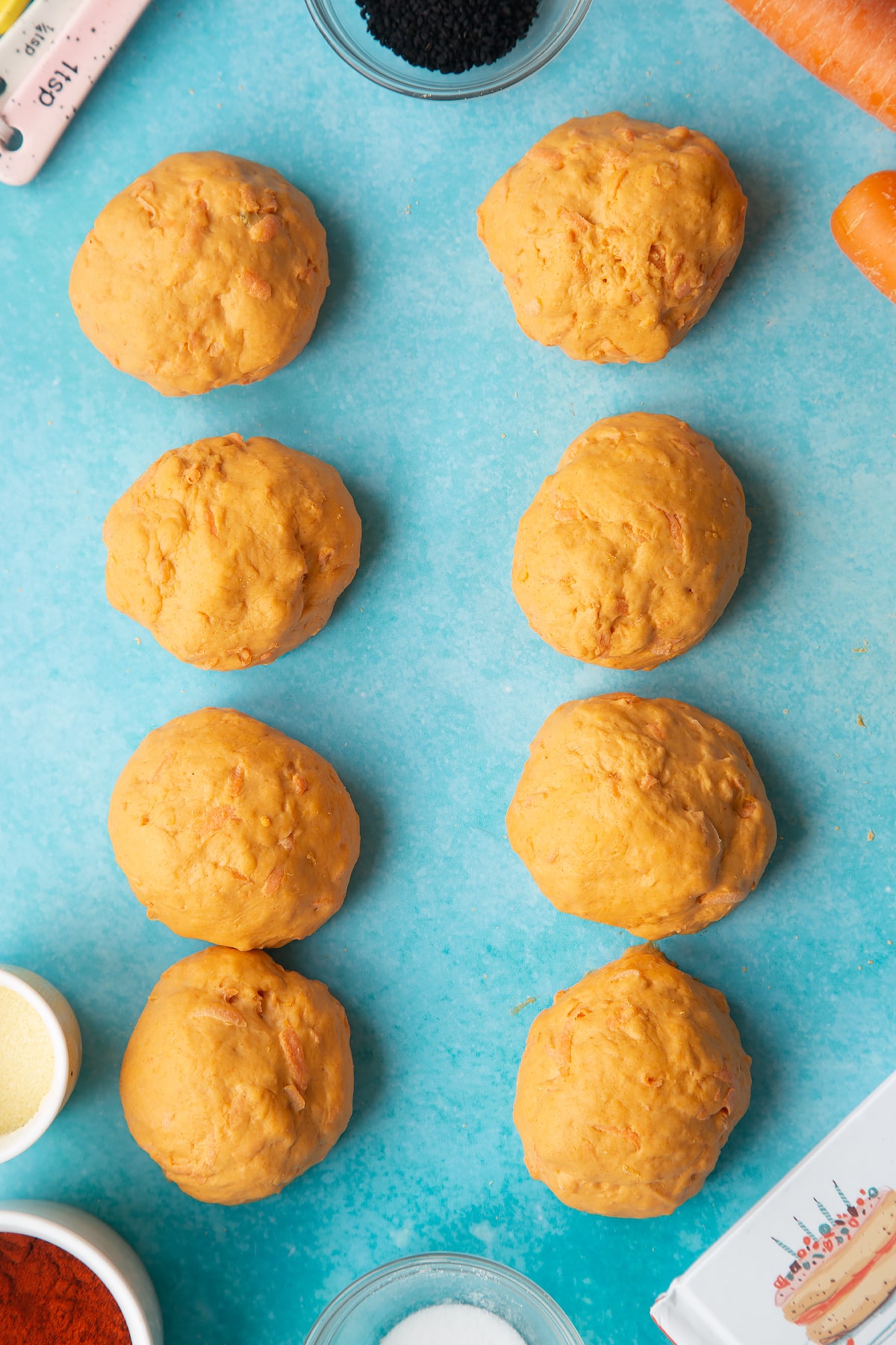 Paprika and carrot bread dough divided into eight pieces. Ingredients to make bread snakes surround the dough.
