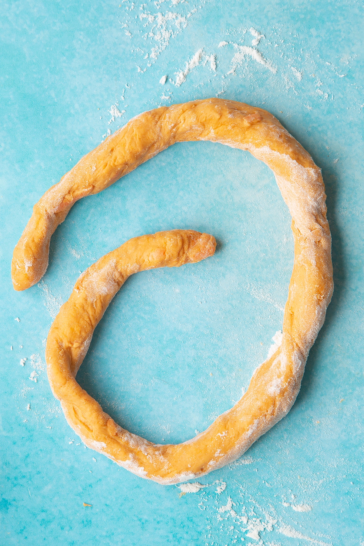 Paprika and carrot bread dough rolled into a long sausage on a floured surface.