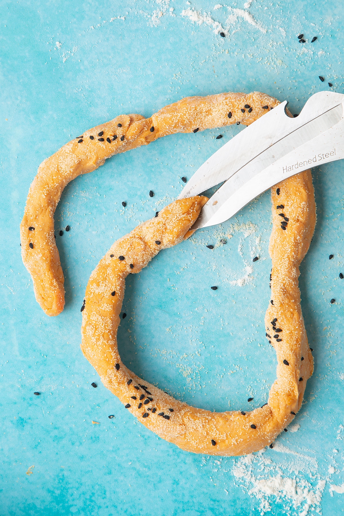 Paprika and carrot bread dough rolled into a long sausage on a floured surface. Scissors snip the end of the dough.