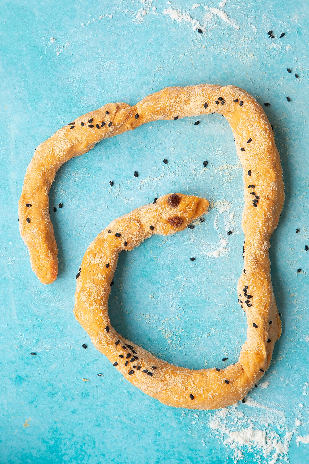 Paprika and carrot bread dough rolled into a long sausage on a floured surface. Two currants have been added to make a mouth.