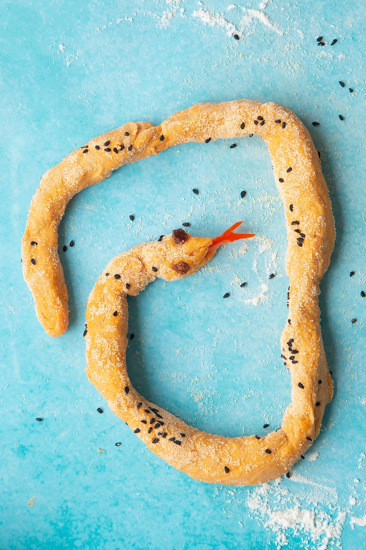 Paprika and carrot bread dough rolled into a long sausage on a floured surface. Red pepper has been added to make a snake's tongue.