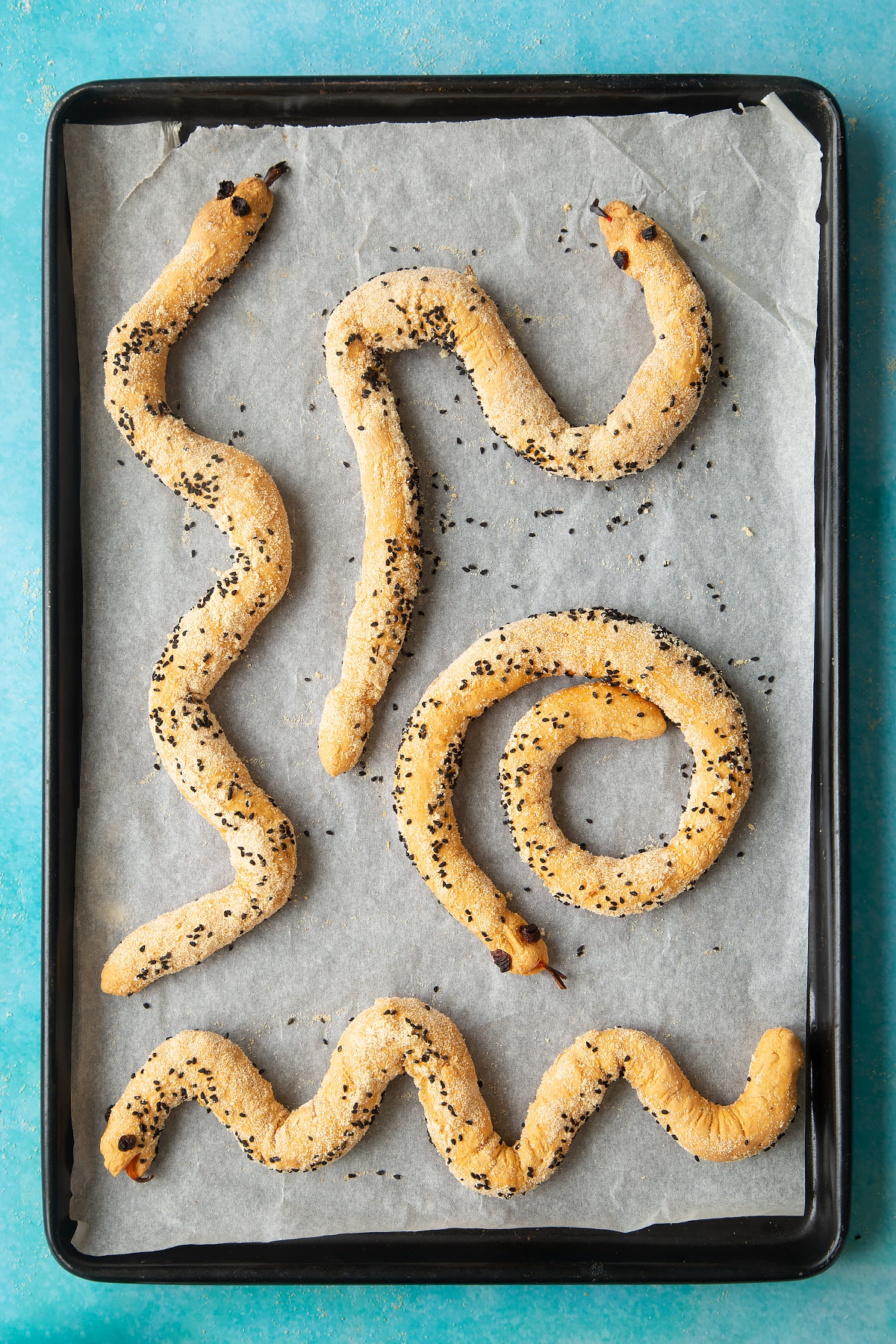 A lined baking tray with freshly baked bread snakes.
