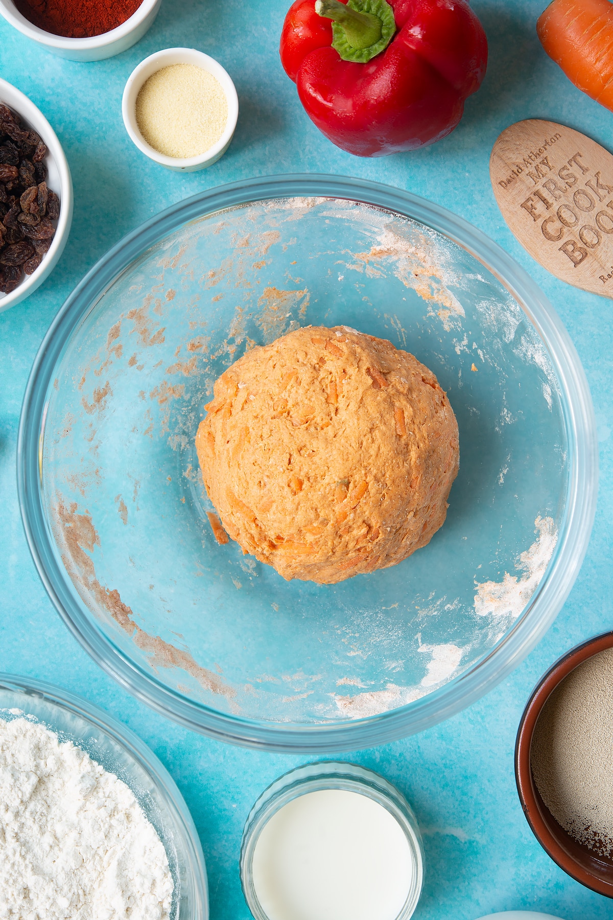Paprika and carrot bread dough in a mixing bowl. Ingredients to make bread snakes surround the bowl.