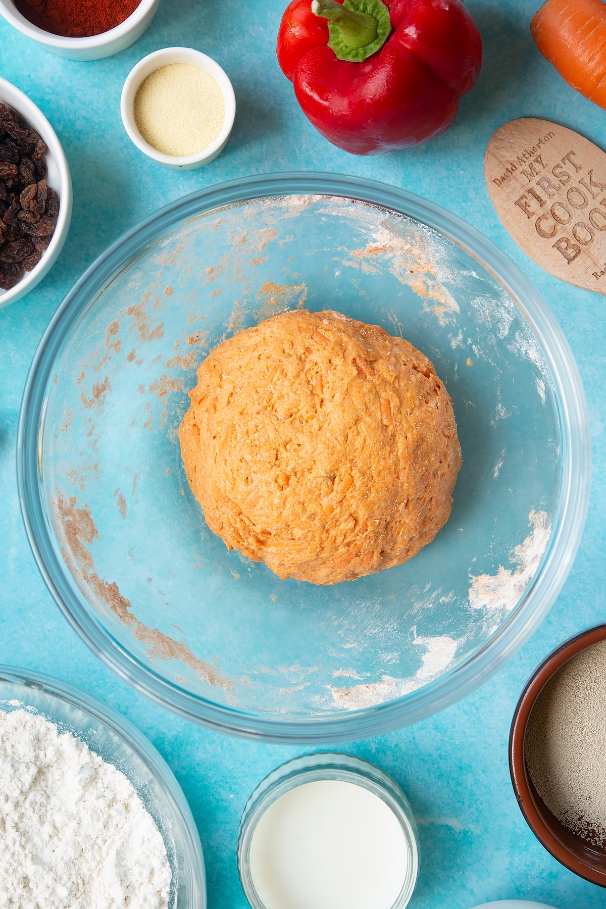 Paprika and carrot bread dough, slightly proved in a mixing bowl. Ingredients to make bread snakes surround the bowl.