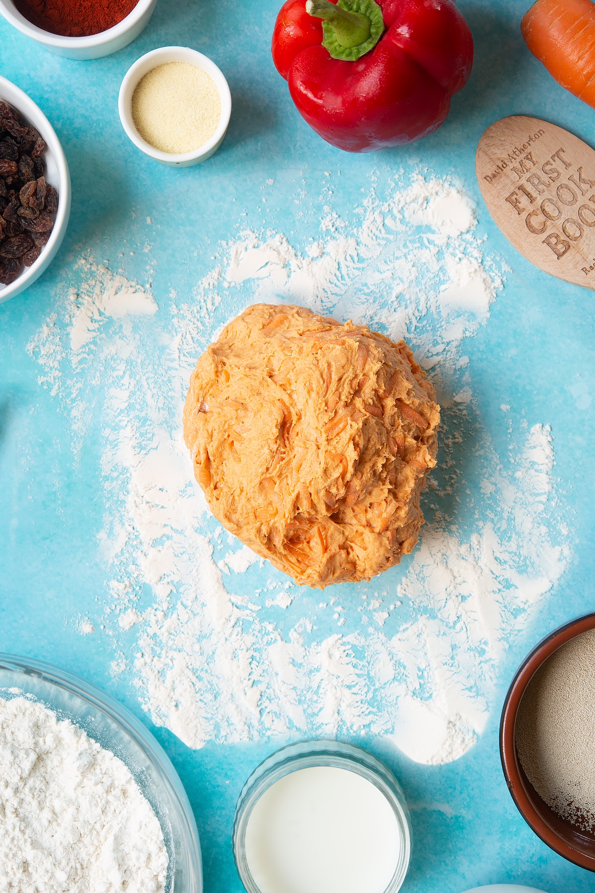 Paprika and carrot bread dough on a floured surface. Ingredients to make bread snakes surround the dough.