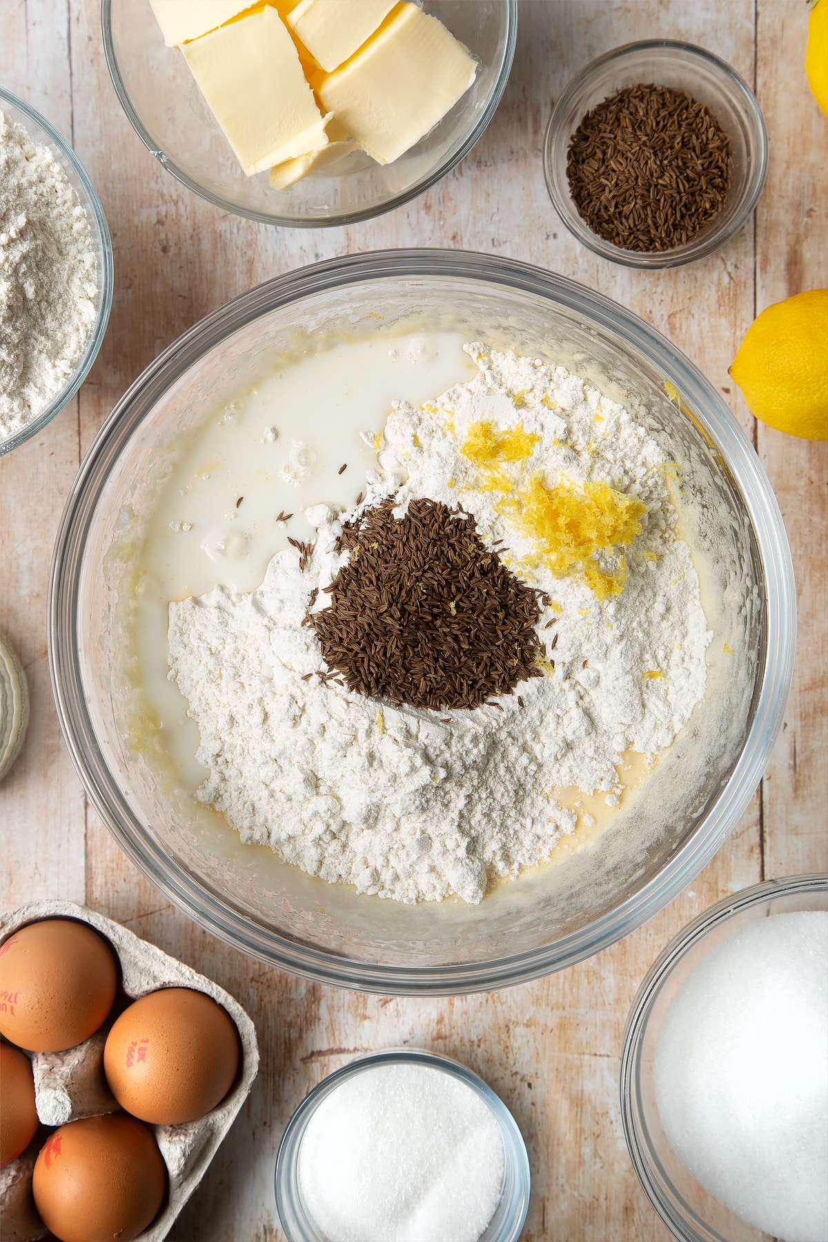 Overhead shot of butter mix, flour, caraway seeds, lemon zest and milk in a clear bowl