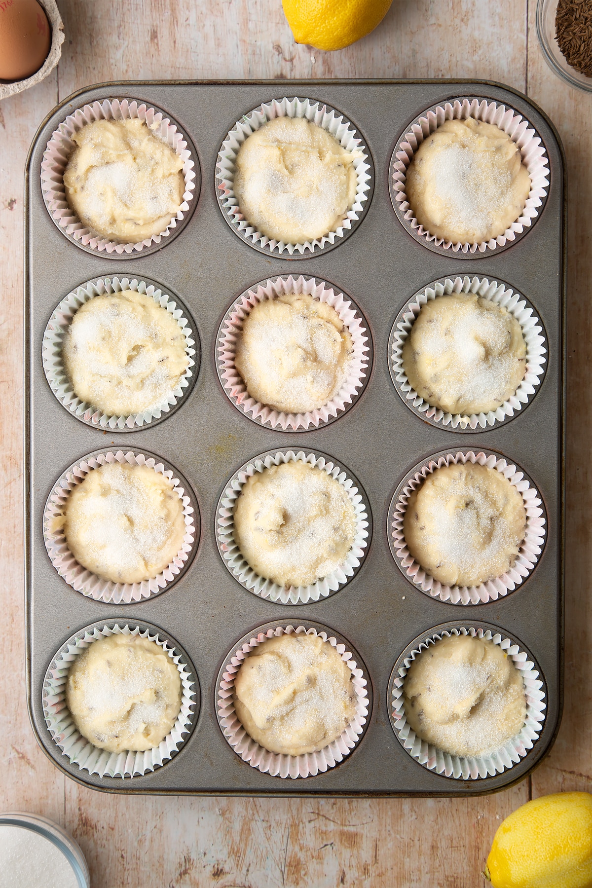 Overhead shot of muffin mix topped with sugar in a 12 hole muffin tray lined with paper cases