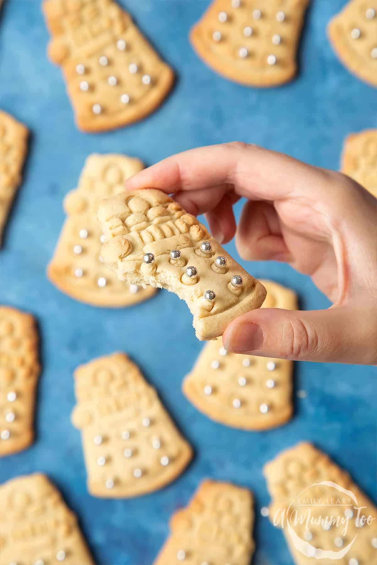Dalek cookies on a blue background. A hand holds one of the Dalek cookies, which has a bite out of it.