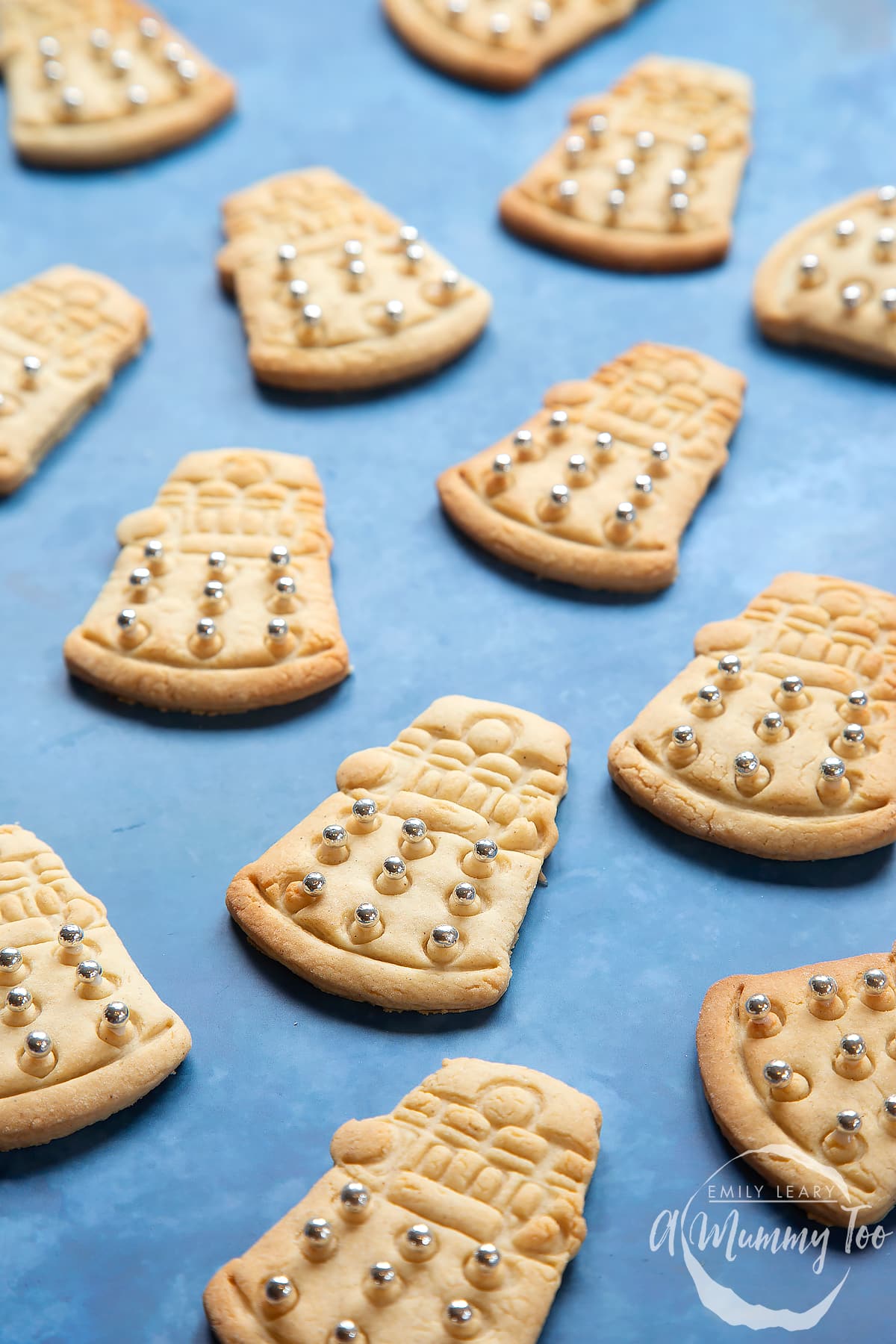 Dalek cookies on a blue background. The cookies are decorated with edible silver candy balls adhered with white icing.
