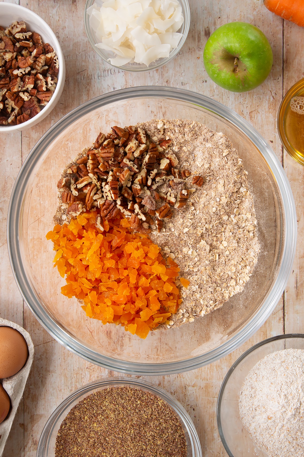 Overhead shot of dry ingredients mix, dried apricots and nuts in a large clear bowl