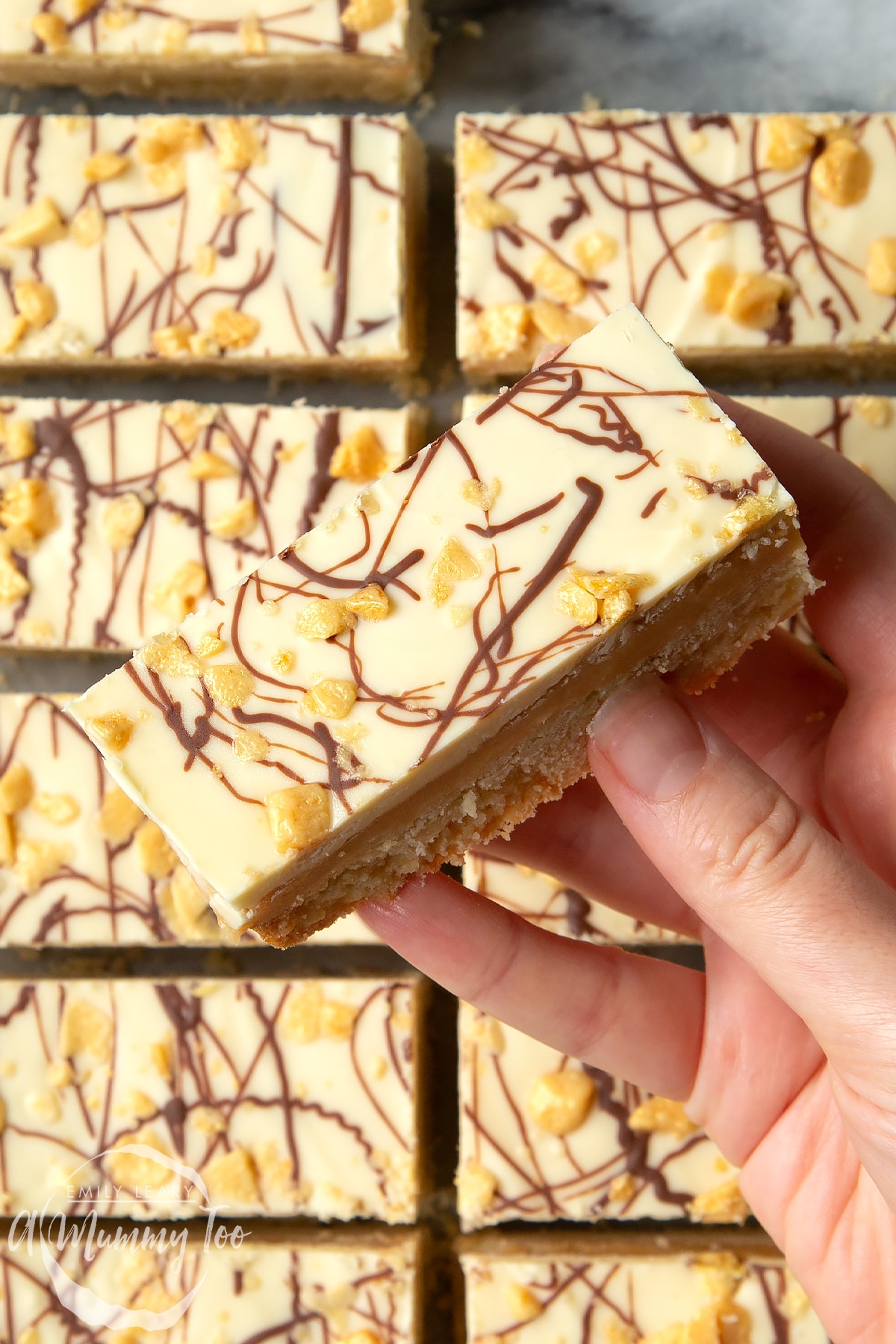 Overhead shot of a hand touching white chocolate shortbread with a mummy too logo in the lower-left corner
