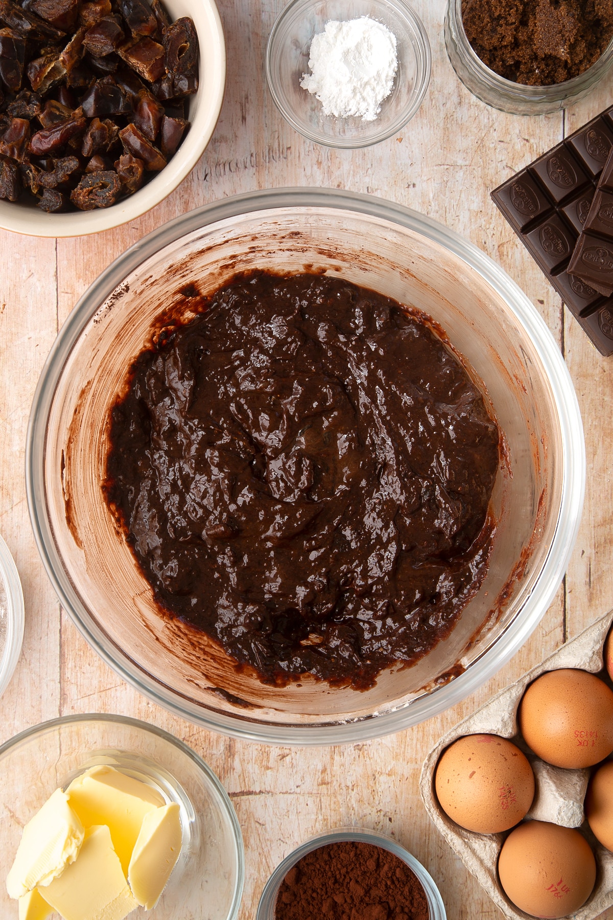 A mixing bowl containing whole grain brownie batter. Ingredients to make whole grain brownies surround the bowl.