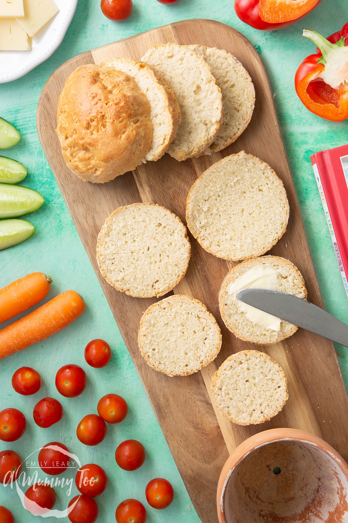 Overhead shot of sliced bread with butter being spread on the slices. Served on a wooden plate with a mummy too logo in the lower-right corner