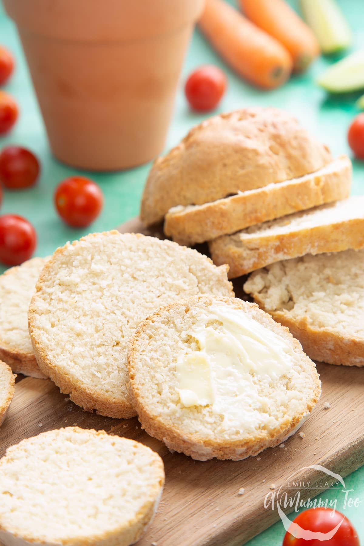 Overhead shot of sliced bread with butter spread served on a wooden plate with a mummy too logo in the lower-right corner