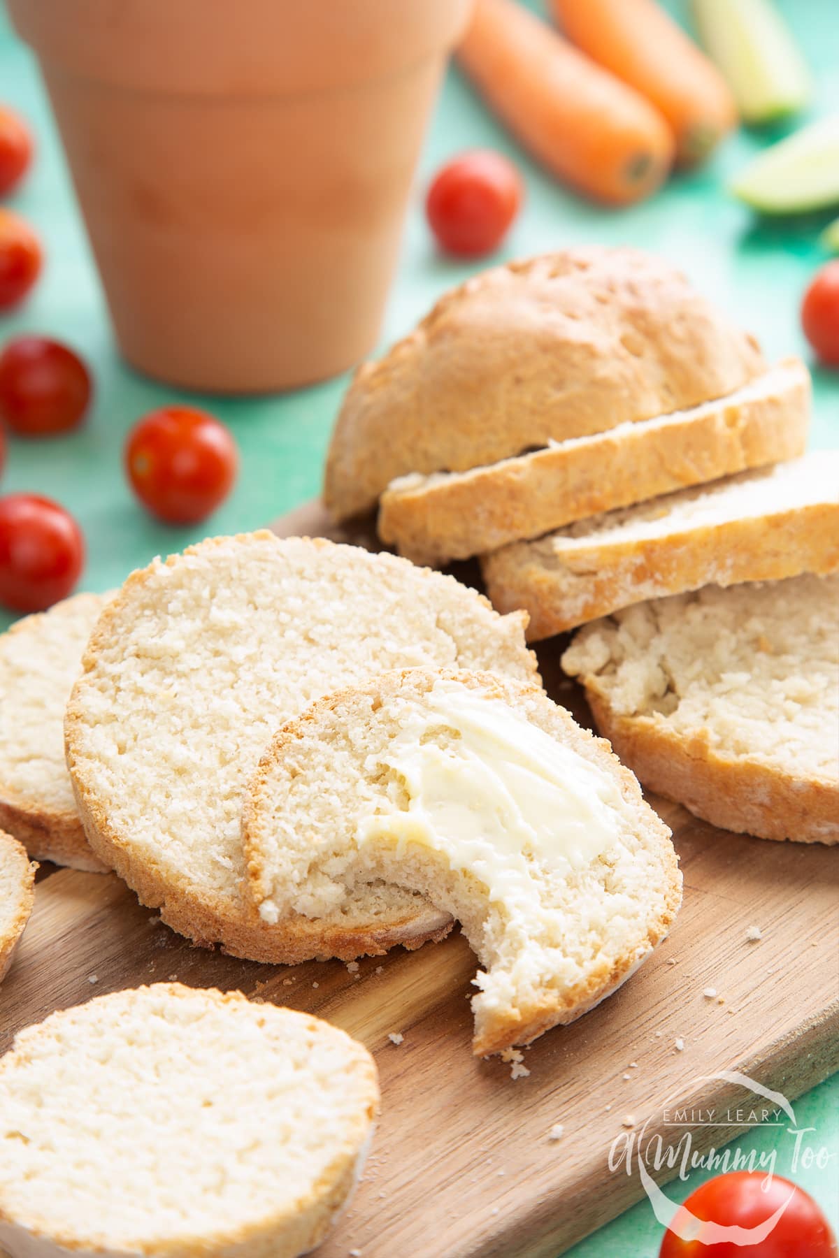 Overhead shot of sliced bread with butter spread served on a wooden plate with a mummy too logo in the lower-right corner