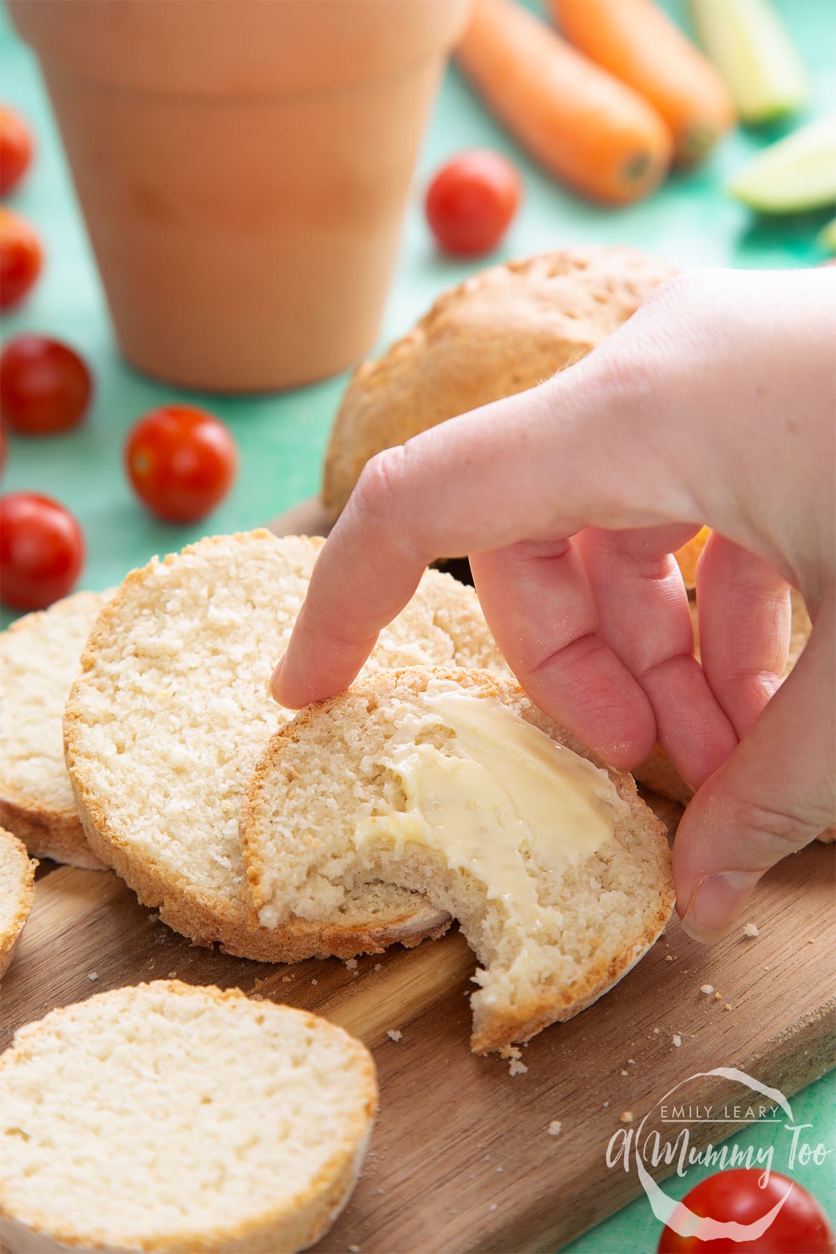 Overhead shot of sliced bread with butter spread served on a wooden plate with a mummy too logo in the lower-right corner