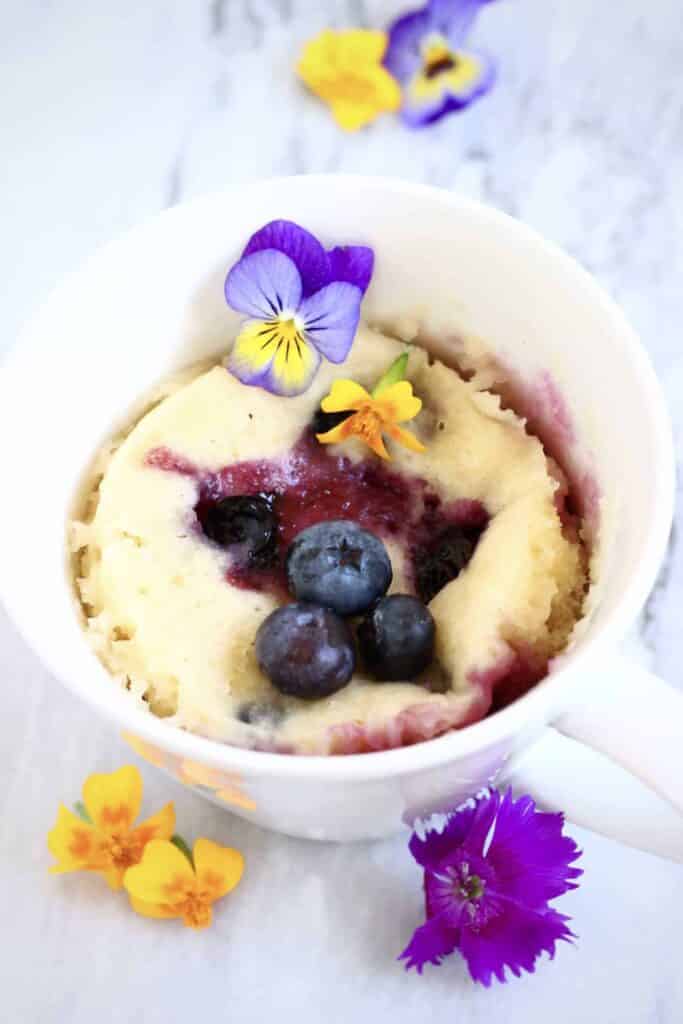 Vegan lemon blueberry mug cake, decorated with fresh blueberries and edible fllowers.