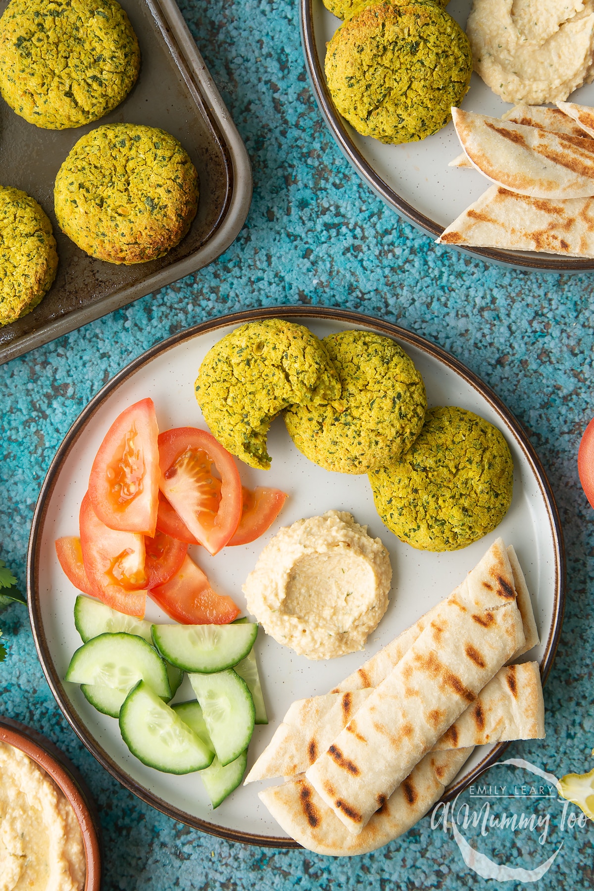 Gluten-free falafel on a plate with tomatoes, cucumber, hummus and griddled flatbread. One of the falafel has a bite out of it.