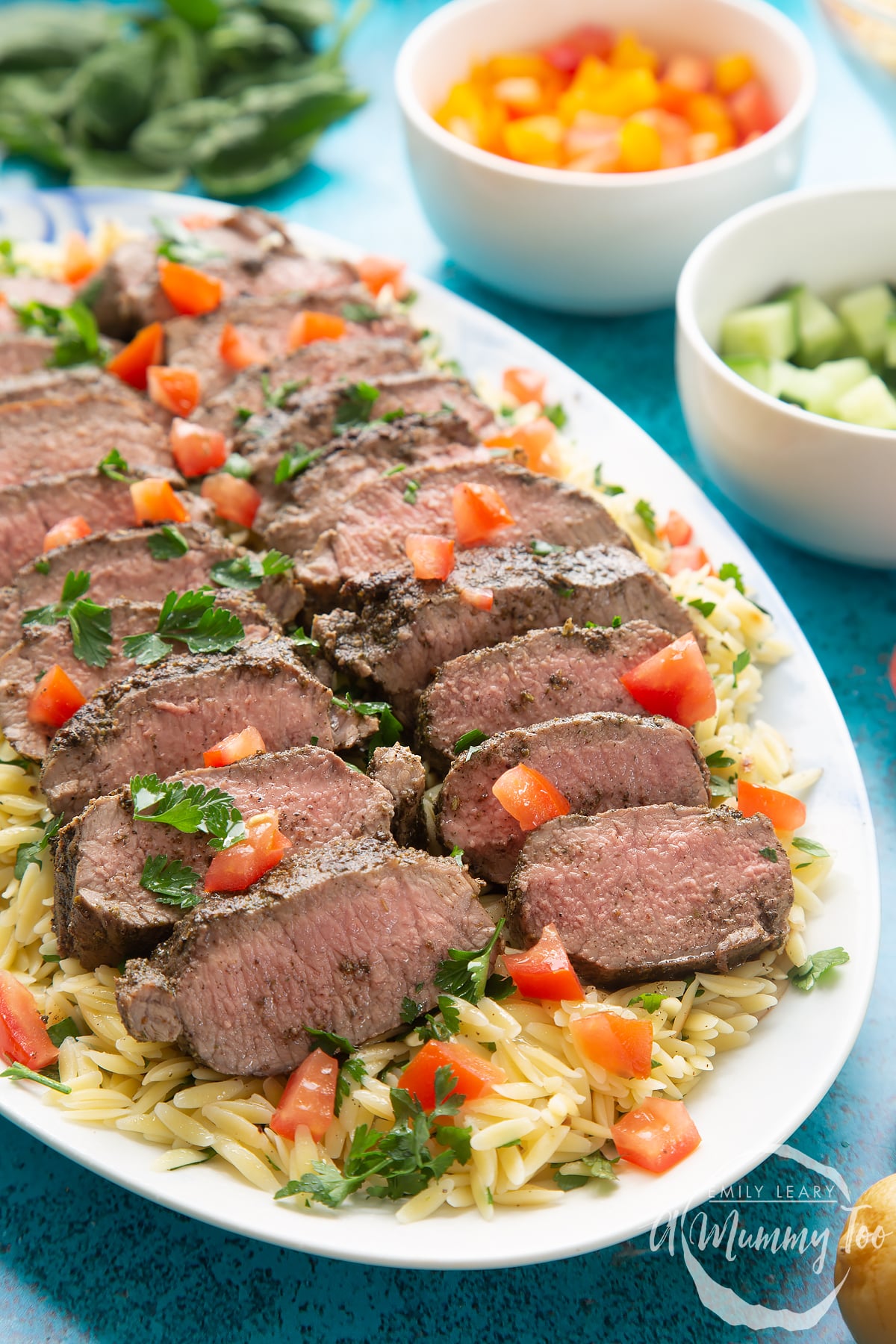 Slices of herby lamb arranged on a bed of orzo on an oval platter.