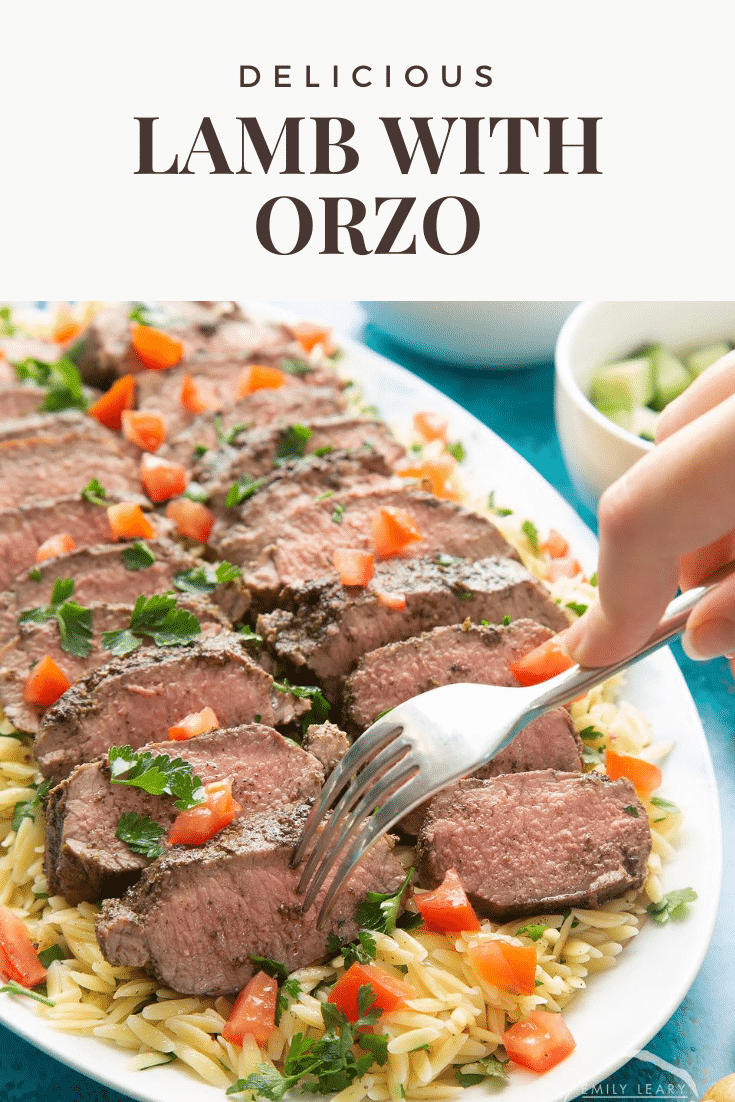 Slices of herby lamb arranged on a bed of orzo on an oval platter. A fork takes some lamb. Caption reads: delicious lamb with orzo