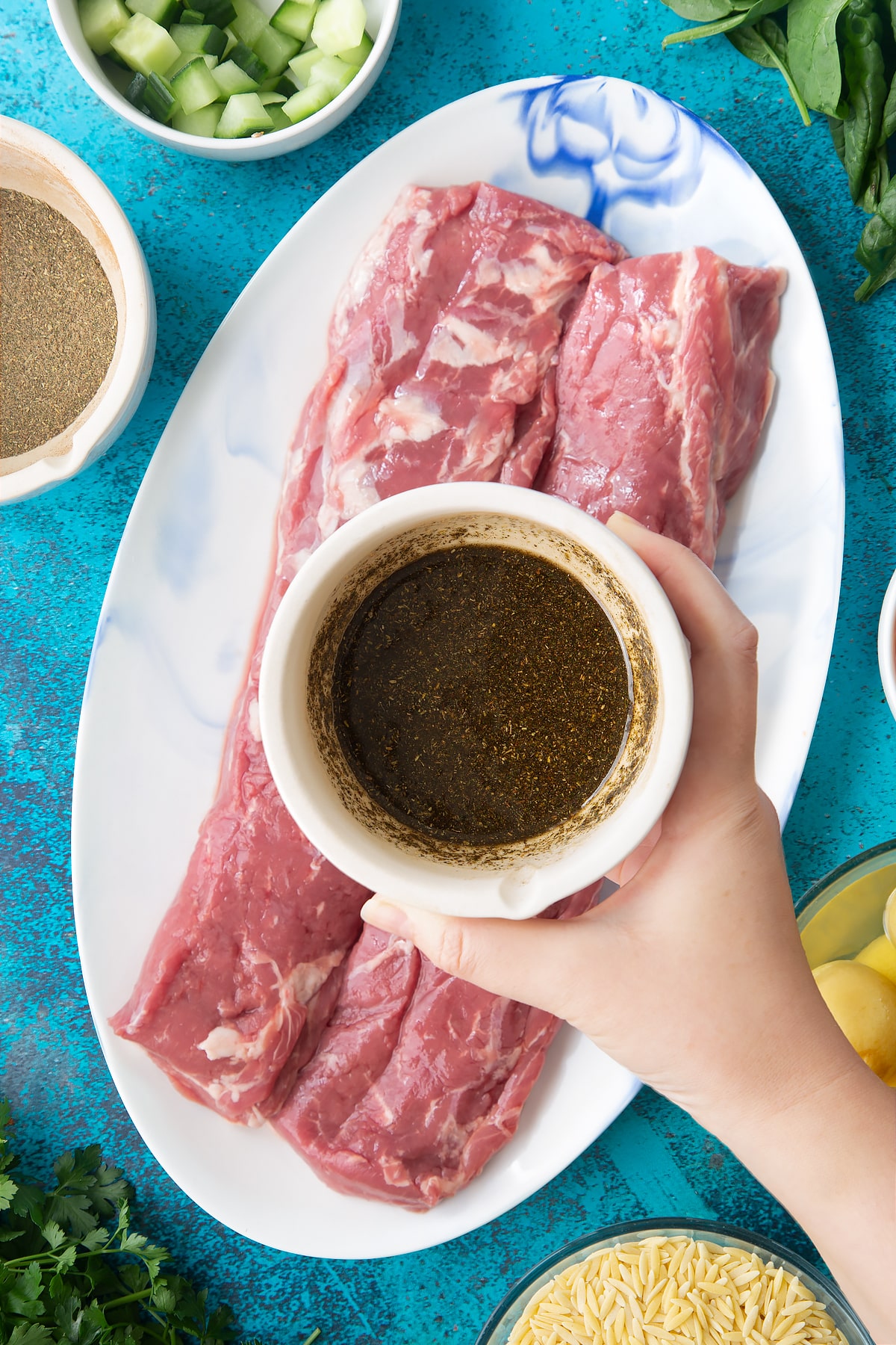 Herb and oil rub in a mortar above two pieces of cannon of Welsh lamb on an oval platter.
