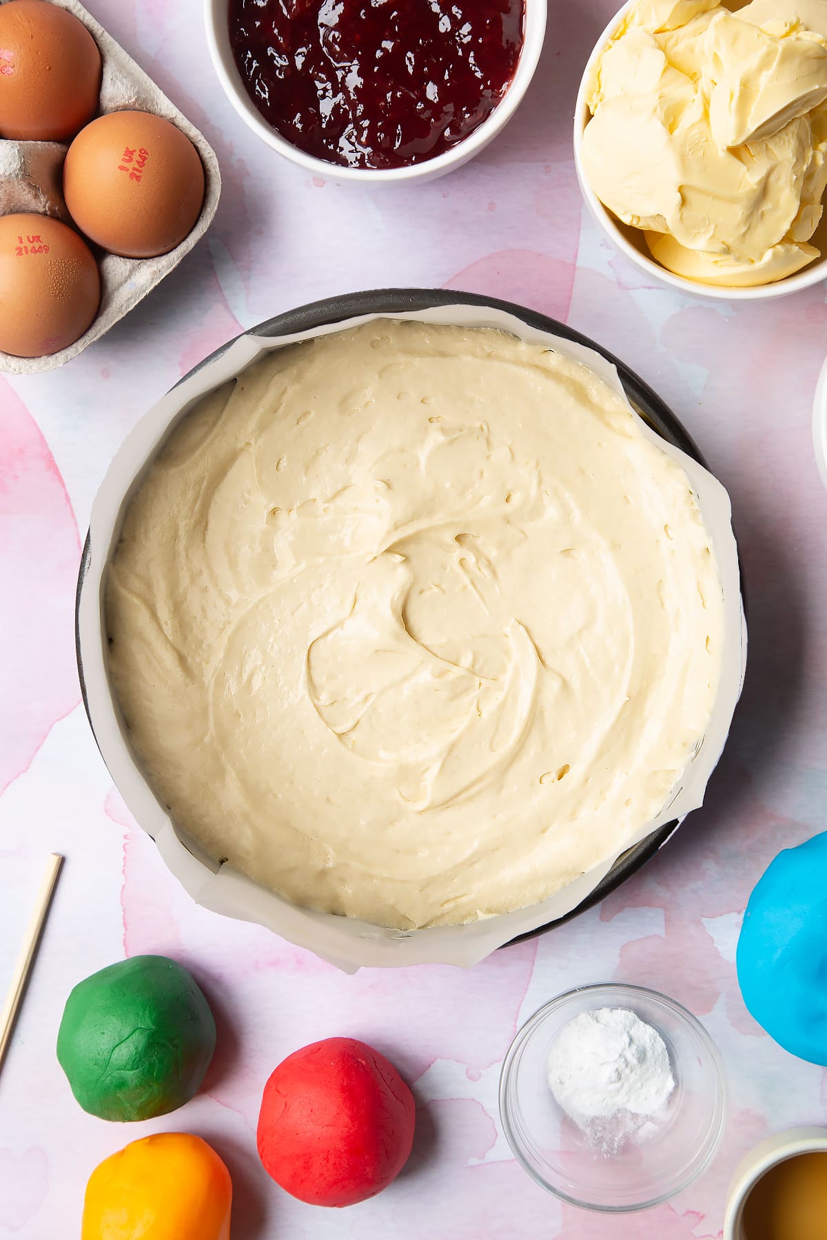 Overhead shot of cake mixture in a cake tin with the coloured sugar paste balls on the side.