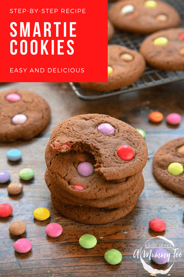 Smartie cookies stacked up on a dark wooden surface. The top cookie has been bitten. Caption reads: step-by-step recipe Smartie cookies easy and delicious