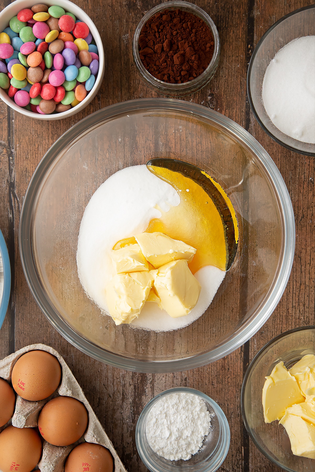 Syrup, sugar and butter in a glass mixing bowl. Ingredients to make the Smartie cookie recipe surround the bowl.