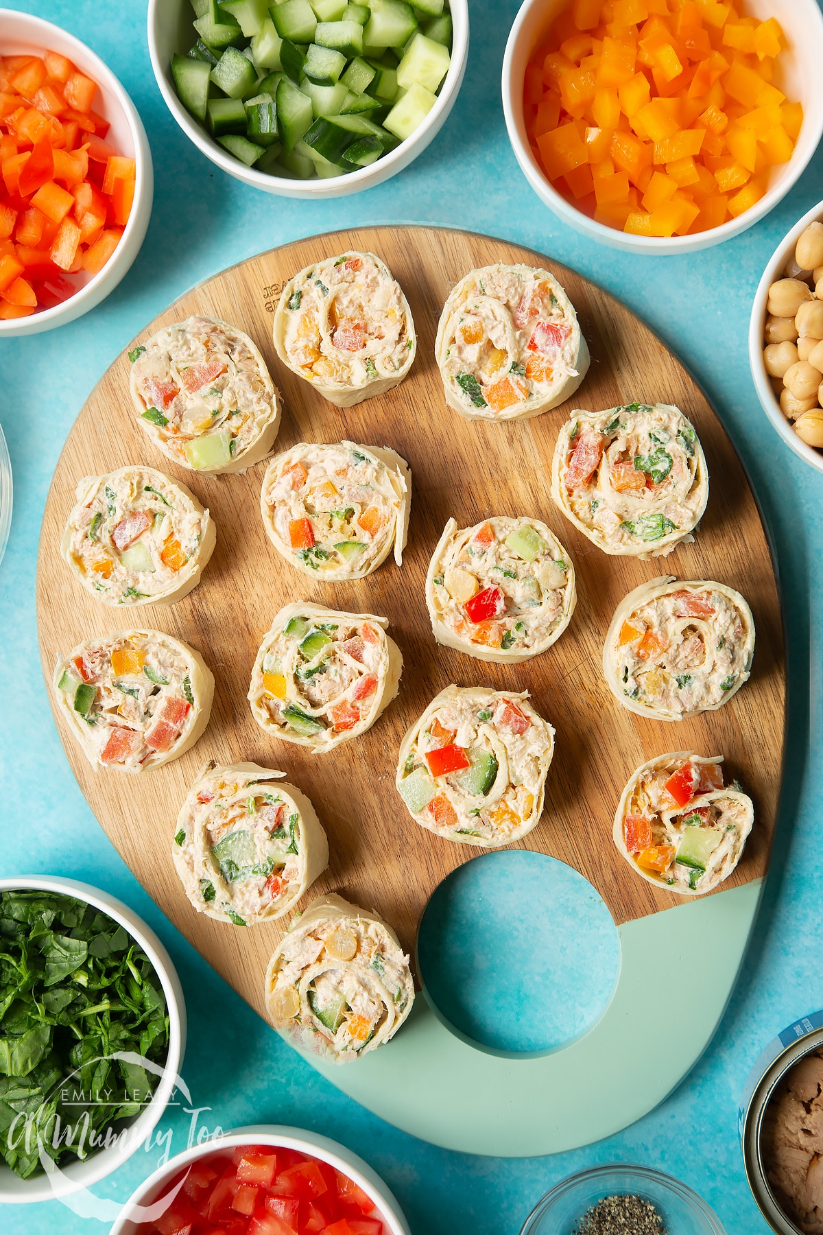 Tuna pinwheels on a wooden board, surrounded by fresh fruit and veg.