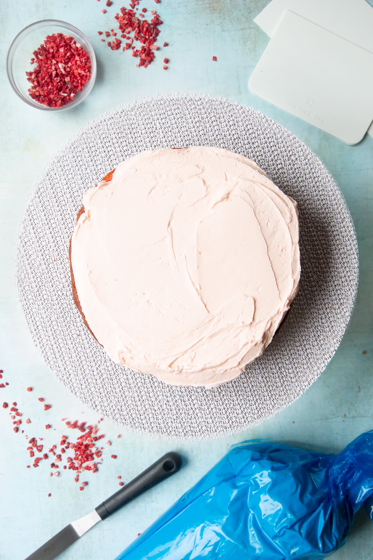 The first layer of a pink ombre cake (the brightest pink shade) topped with pale pink frosting on a cake turntable.