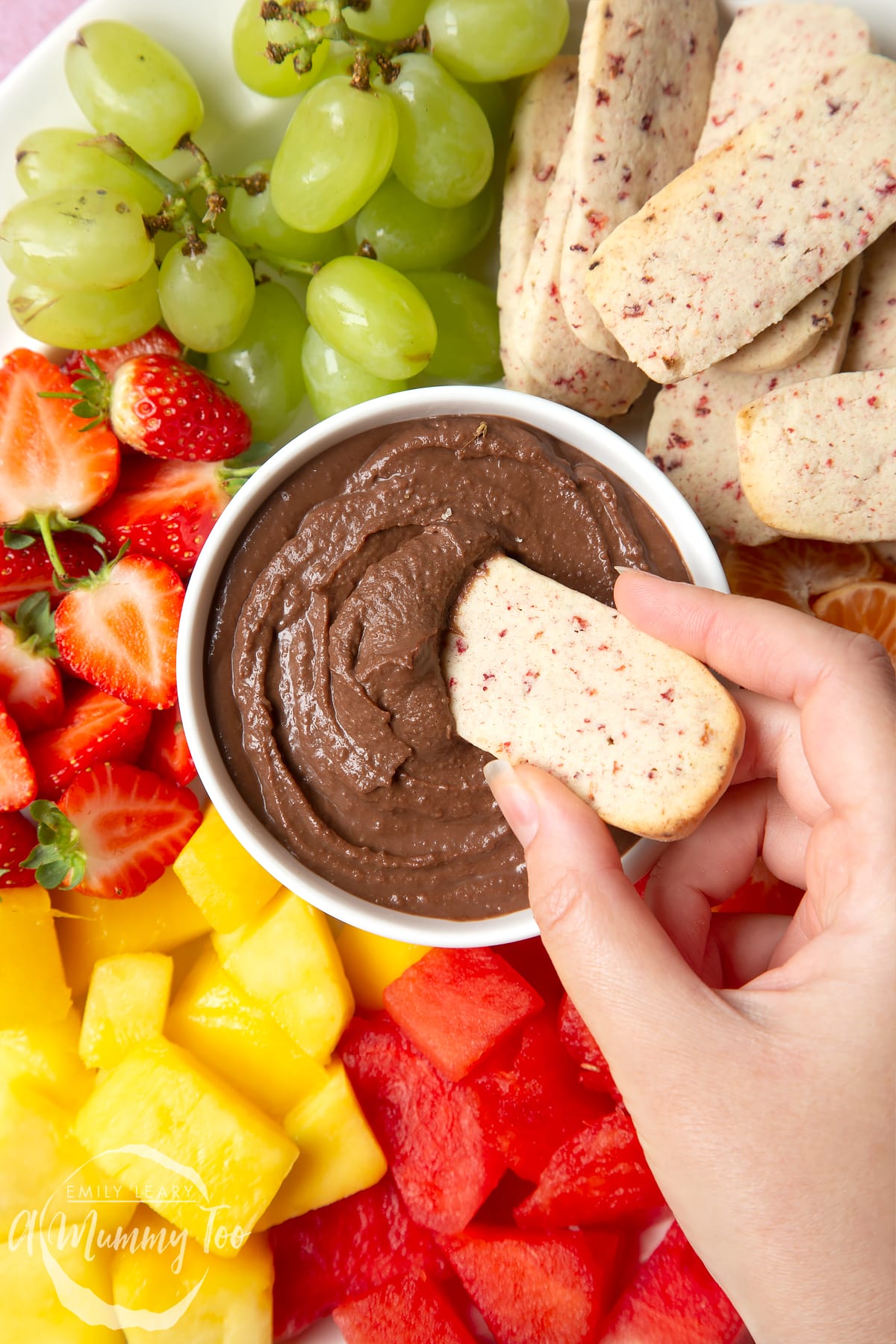 Strawberry biscuits surrounded by grapes, strawberries, mango and watermelon with a chocolate dip in the center.