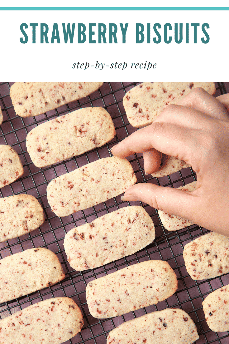 Strawberry biscuits on a wire rack cooling being picked up by a hand. At the top of the image there's some text.