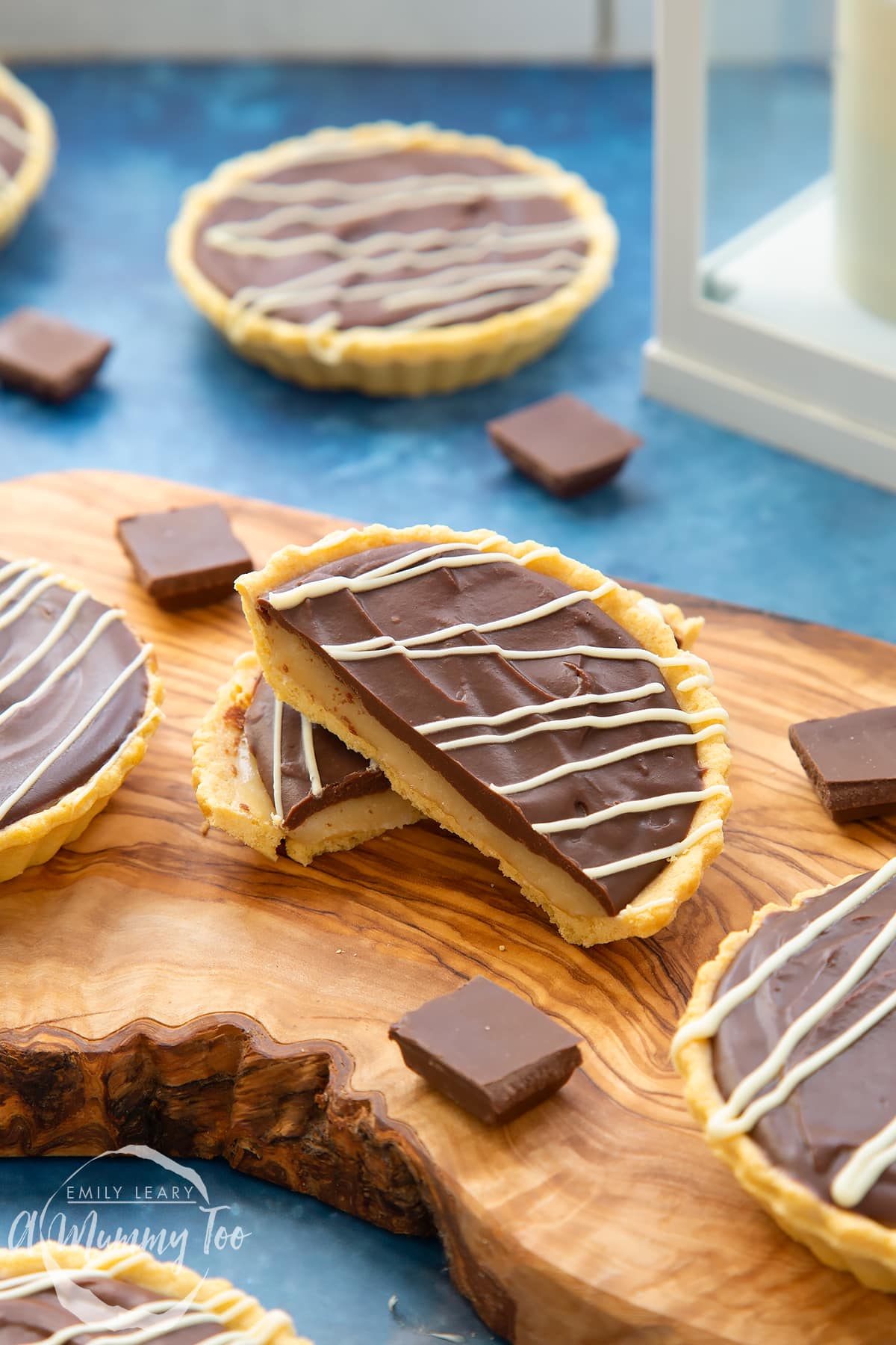 Mini chocolate tarts on an olive board. The tart in focus has been cut in half.