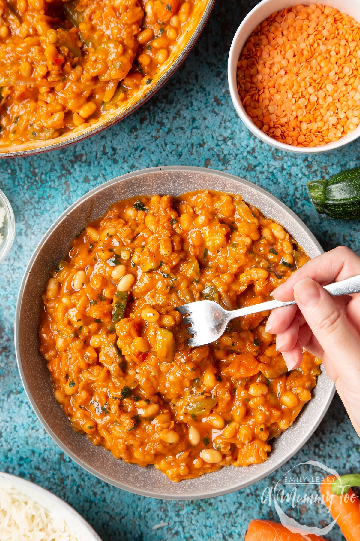 Baked bean curry served in a grey bowl. A hand dips a fork into the curry.