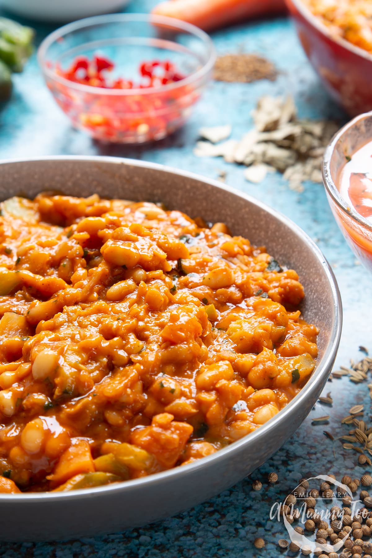 Baked bean curry served in a grey bowl. Chilli and other ingredients show in the background.