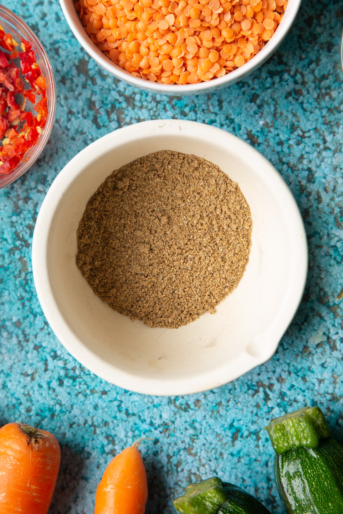Ground spices in a mortar. Ingredients to make baked bean curry surround the mortar.