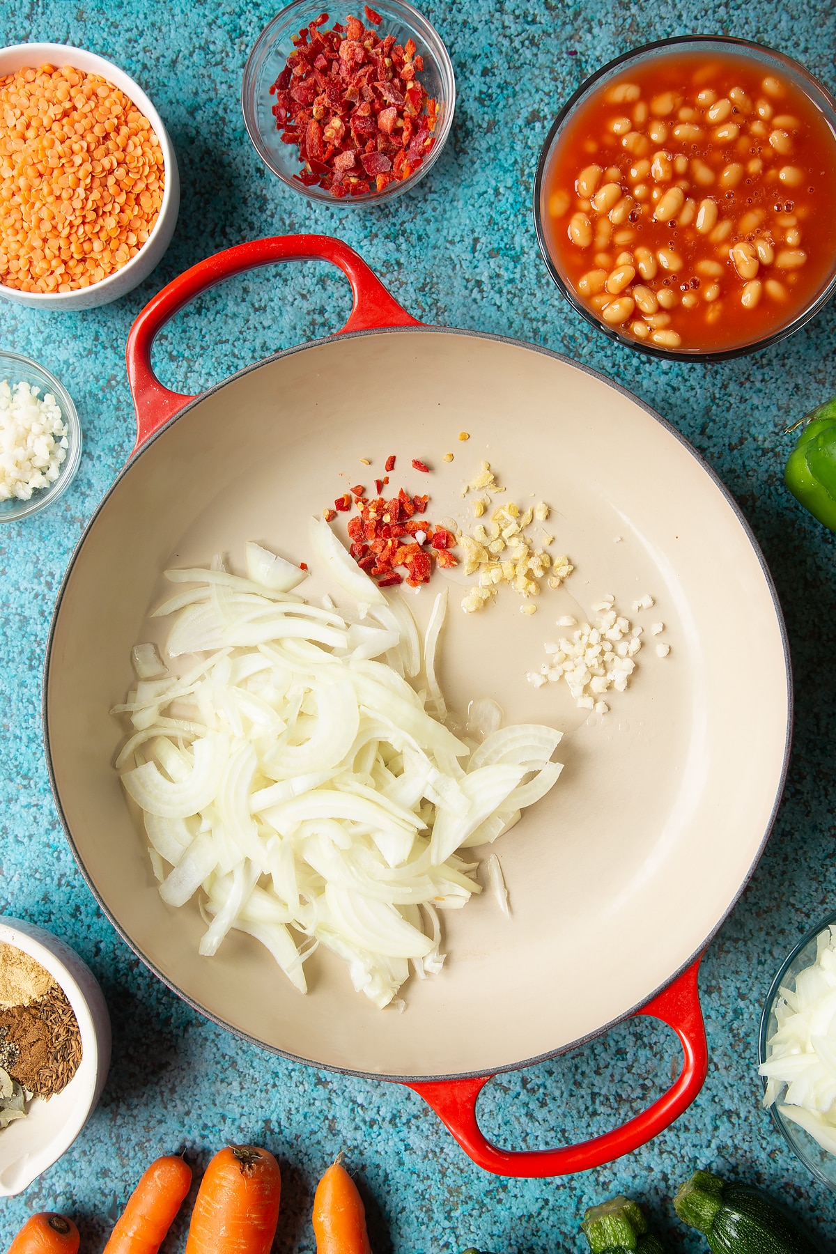 Onions, chilli, ginger, garlic and oil in a pan. Ingredients to make baked bean curry surround the pen.