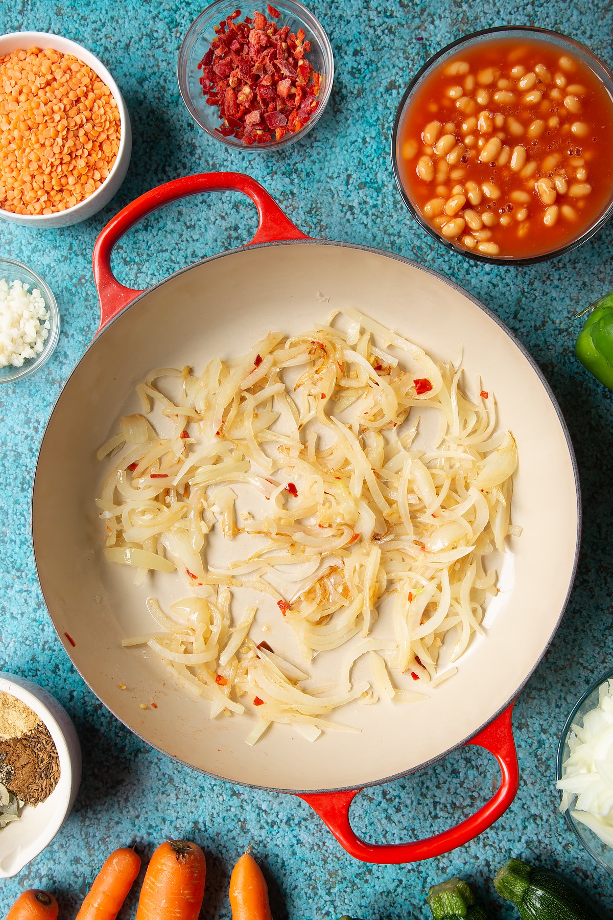 Fried onions, chilli, ginger and garlic in a pan. Ingredients to make baked bean curry surround the pen.