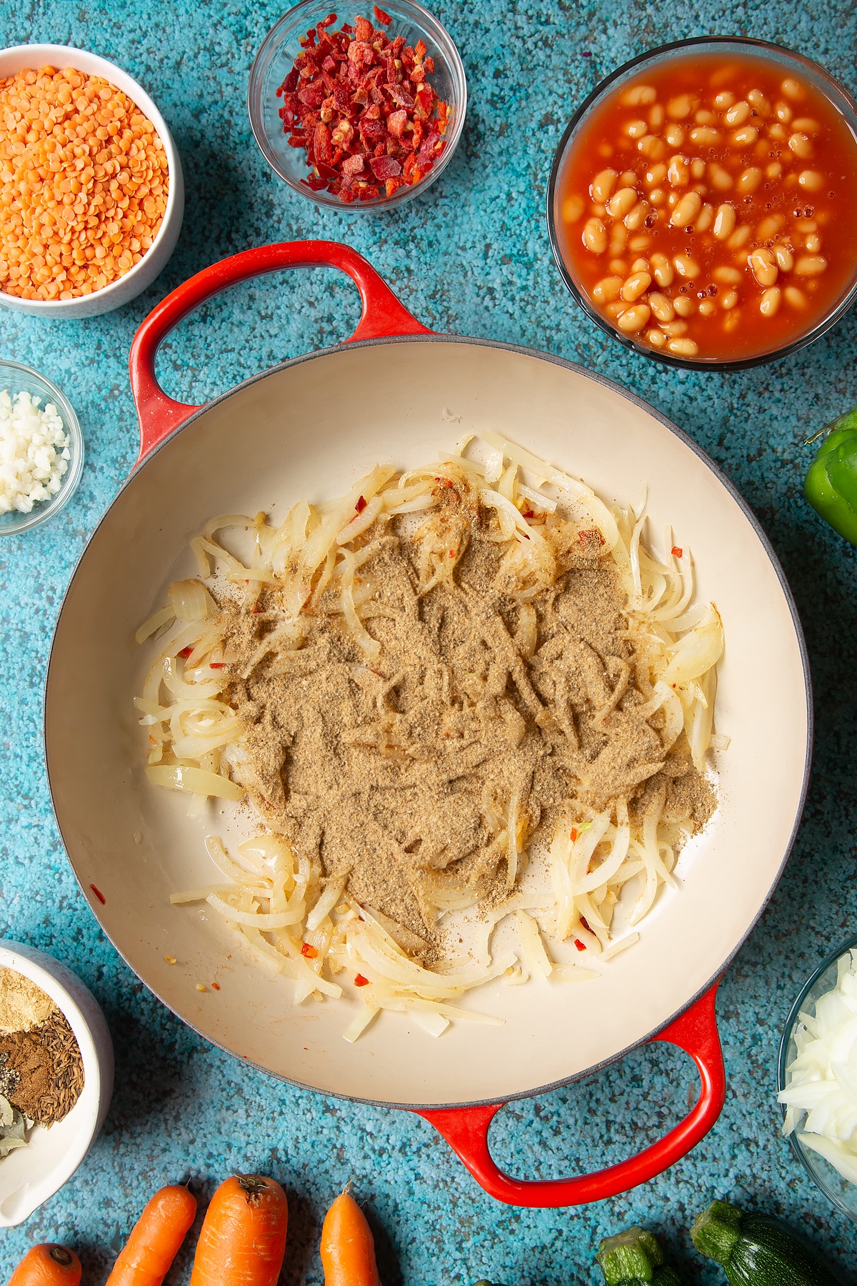 Fried onions, chilli, ginger and garlic in a pan with a spice blend on top. Ingredients to make baked bean curry surround the pen.