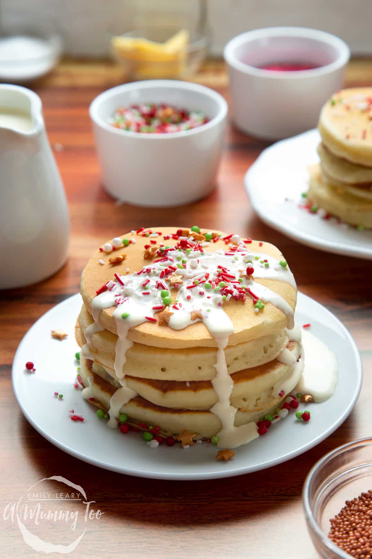 Christmas morning pancakes, stacked on a white plate, drizzled with cream and scattered with festive sprinkles.