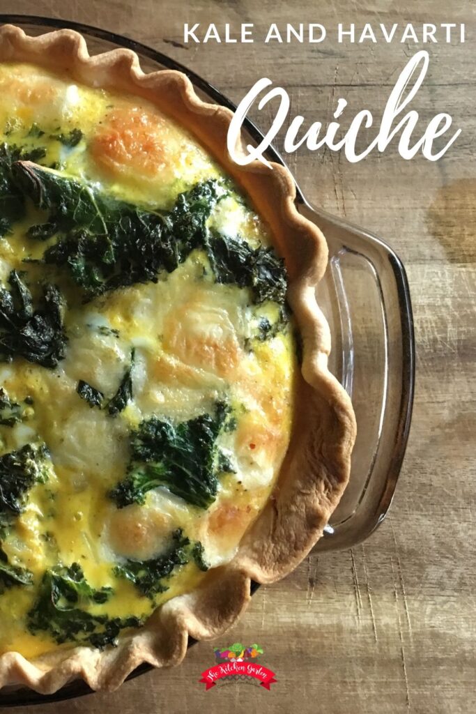 A whole kale and havarti quiche sites inside a ceramic dish on top of a wooden chopping board. The quiche is situated to the left of the image and cuts off the edes.
