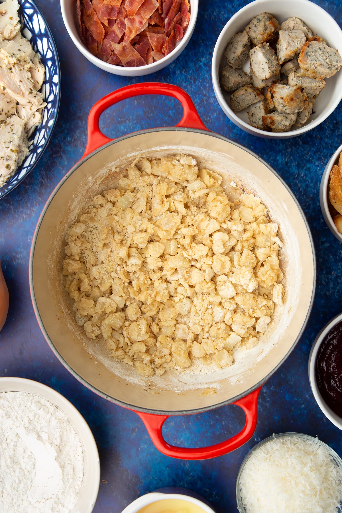 Fried onions coated in flour in a pan. Ingredients to make a leftover Christmas dinner pie surround the pan.