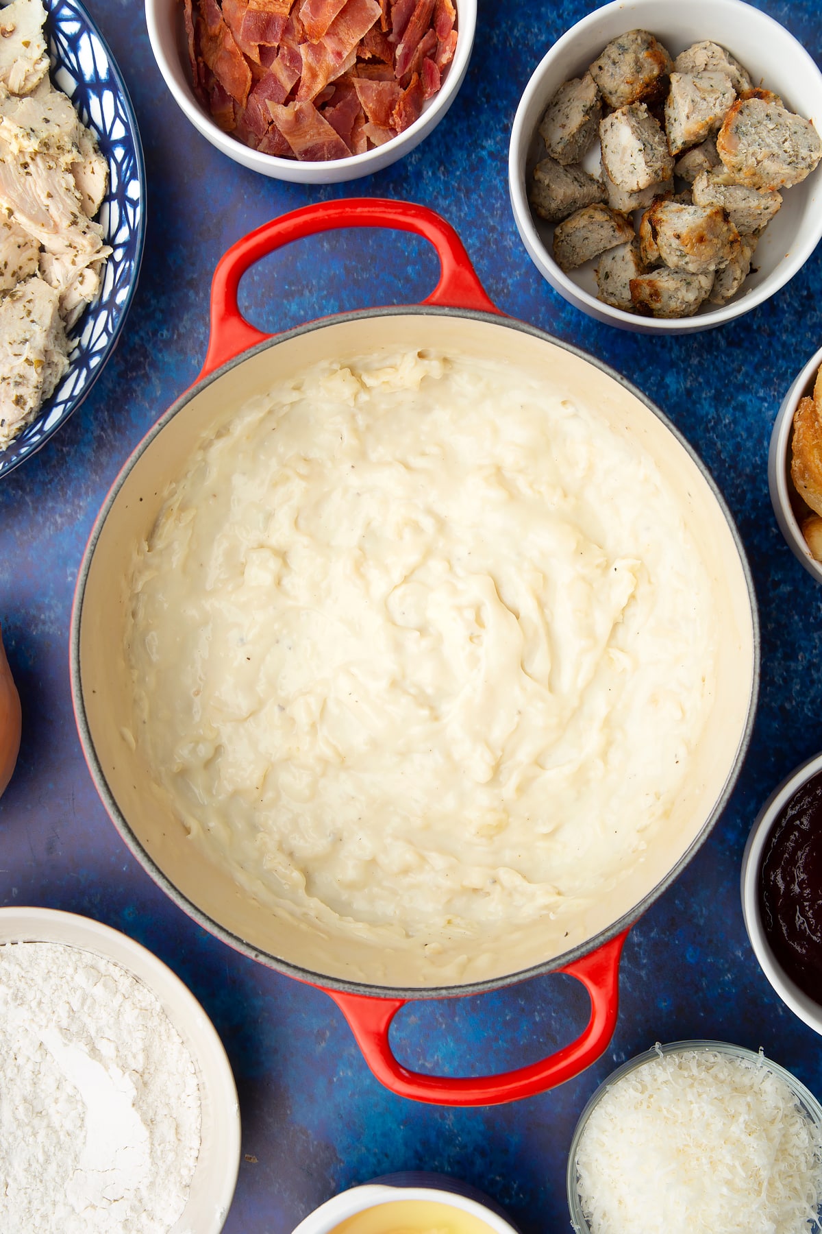 Fried onions in a thick milk sauce in a pan. Ingredients to make a leftover Christmas dinner pie surround the pan.