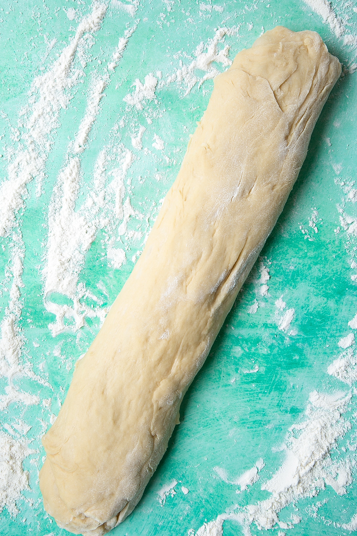 Bread dough rolled into a sausage on a floured surface.