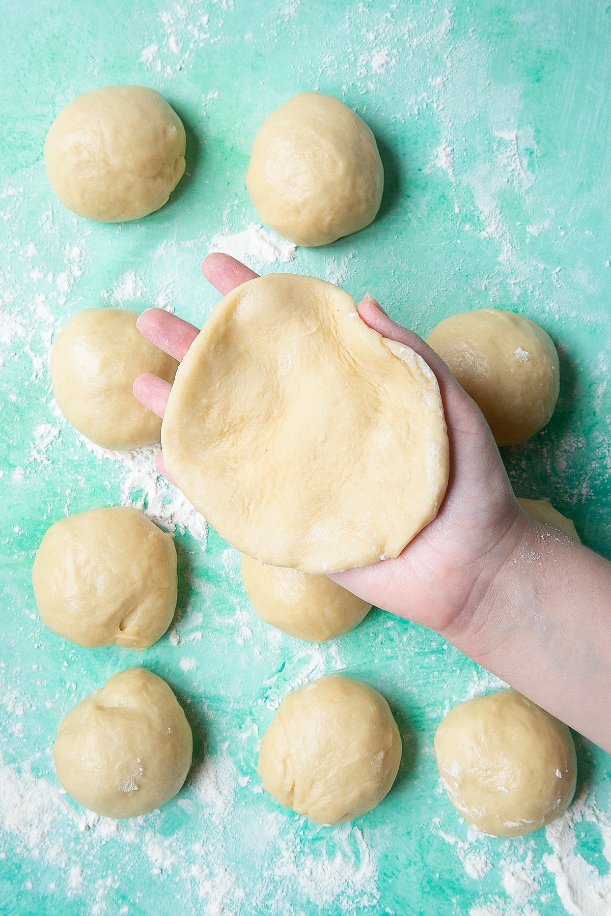 A hand holding a flatten round of bread dough about 12cm (4 3/4 inches) diameter.