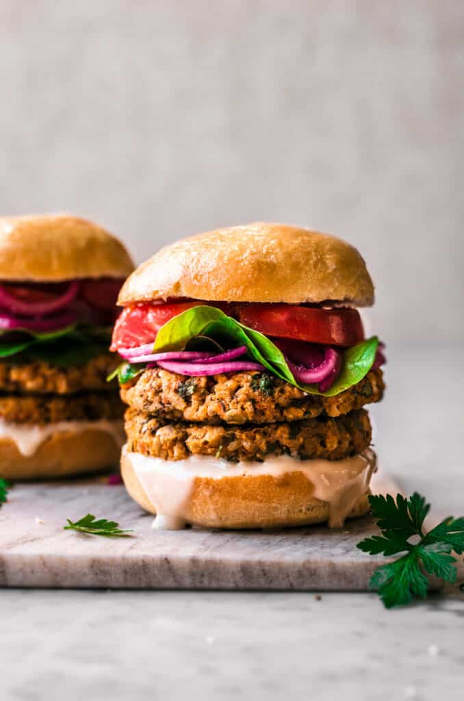 Chickpea Sweet Potato Burgers are double stacked and served on a marble chopping board. There are two burgers sat alongside one and other.