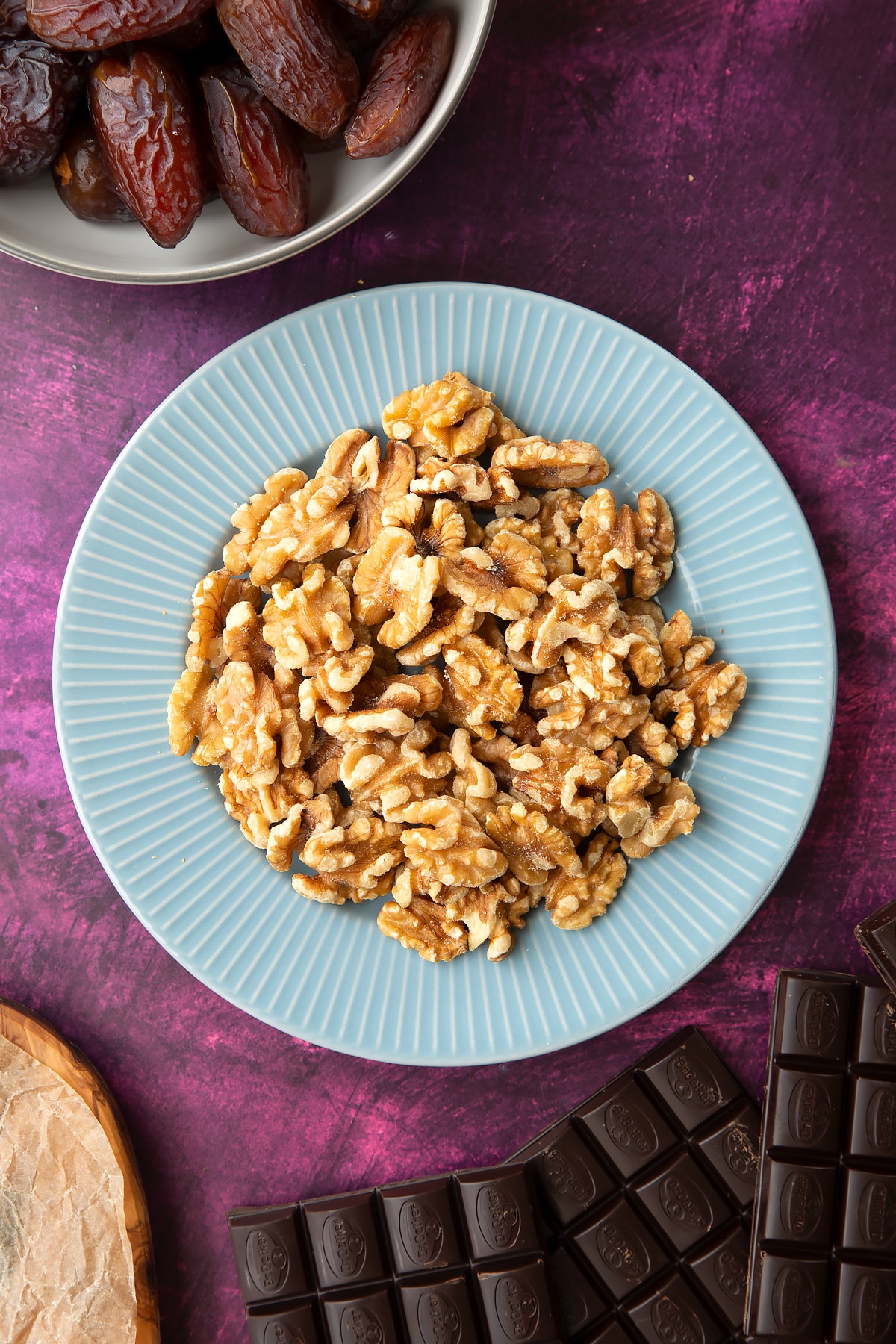 Walnut halves on a blue plate, surrounded by ingredients to make chocolate dates.