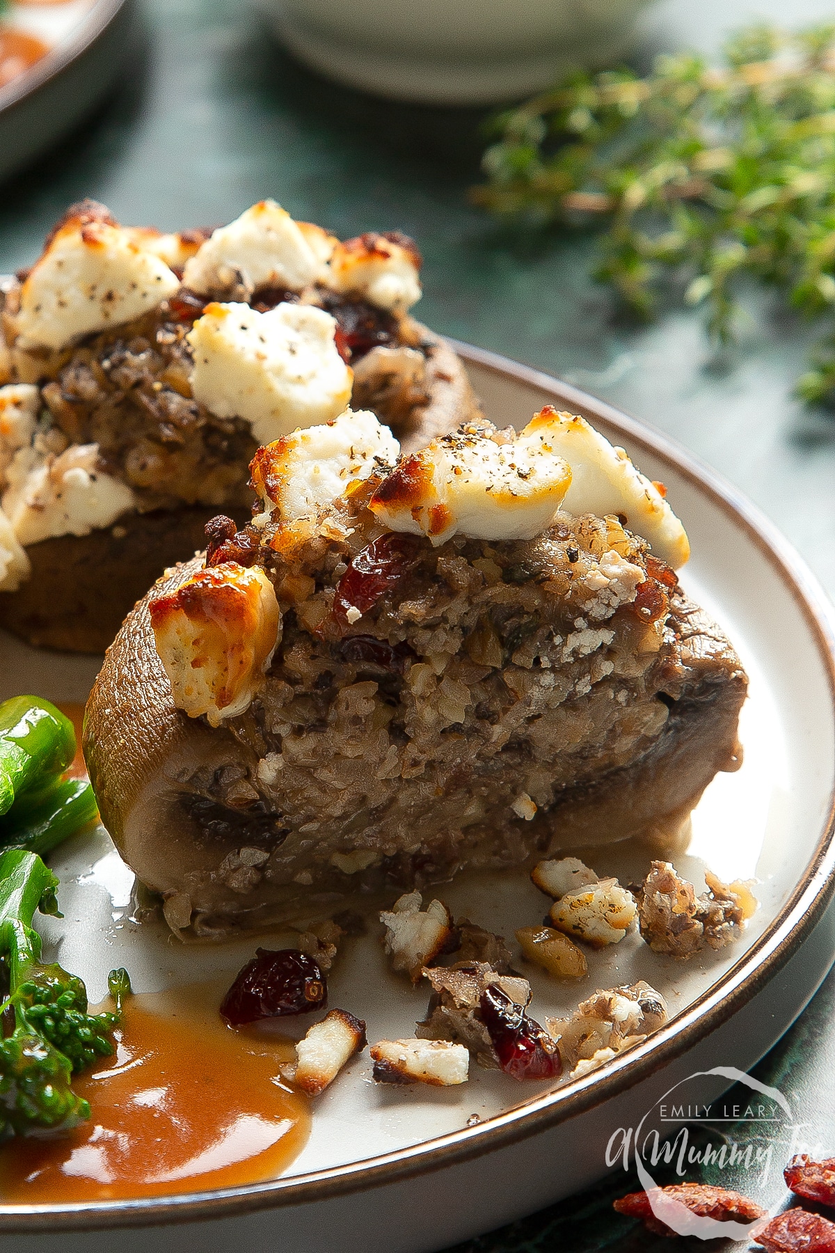 Front angle shot of halved Christmas stuffed mushrooms topped with cheese served on a gray plate with a mummy too logo in the lower-right corner